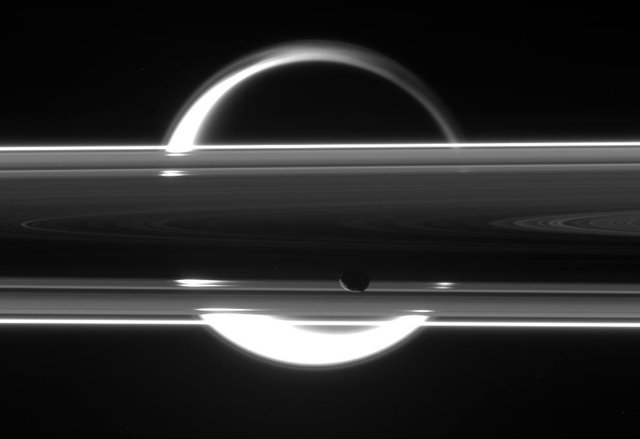 Один из малых спутников, Янус, на фоне кольца, за которым не в фокусе виден крупнейший спутник - Титан. NASA/JPL-Caltech